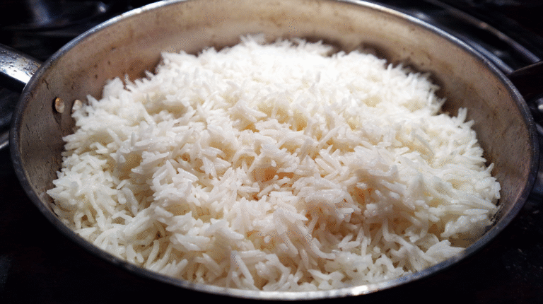 A close-up of cooked white rice in a metal pan, perfectly fluffy thanks to the best water to rice ratio and precise rice cooking instructions for water.