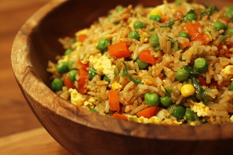 A wooden bowl filled with fried rice containing peas, carrots, corn, scrambled eggs, and green onions.